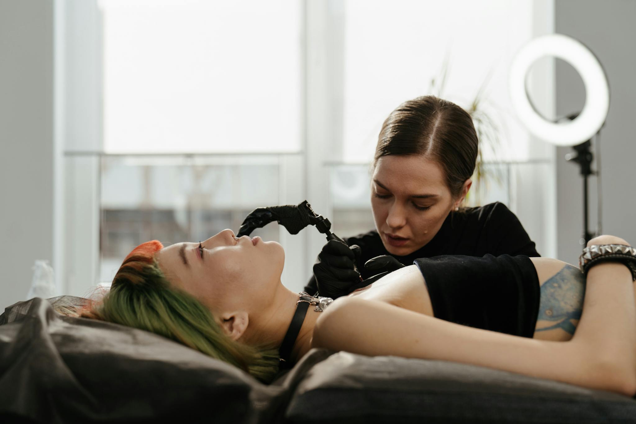 A skilled tattoo artist intricately inking a design on a client's arm in a well-lit, modern studio.