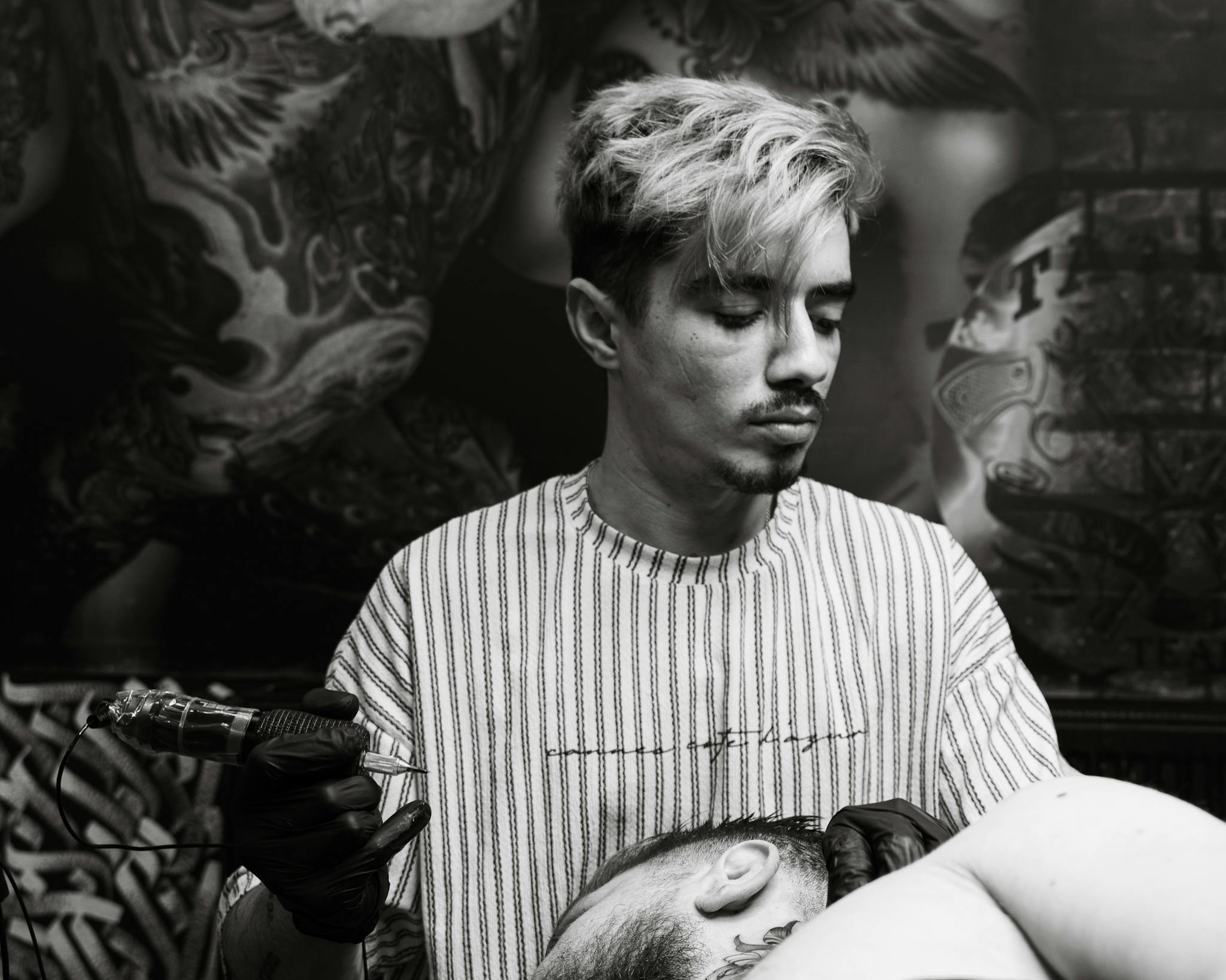 Black and white image of a tattoo artist focused on work, showcasing studio atmosphere.
