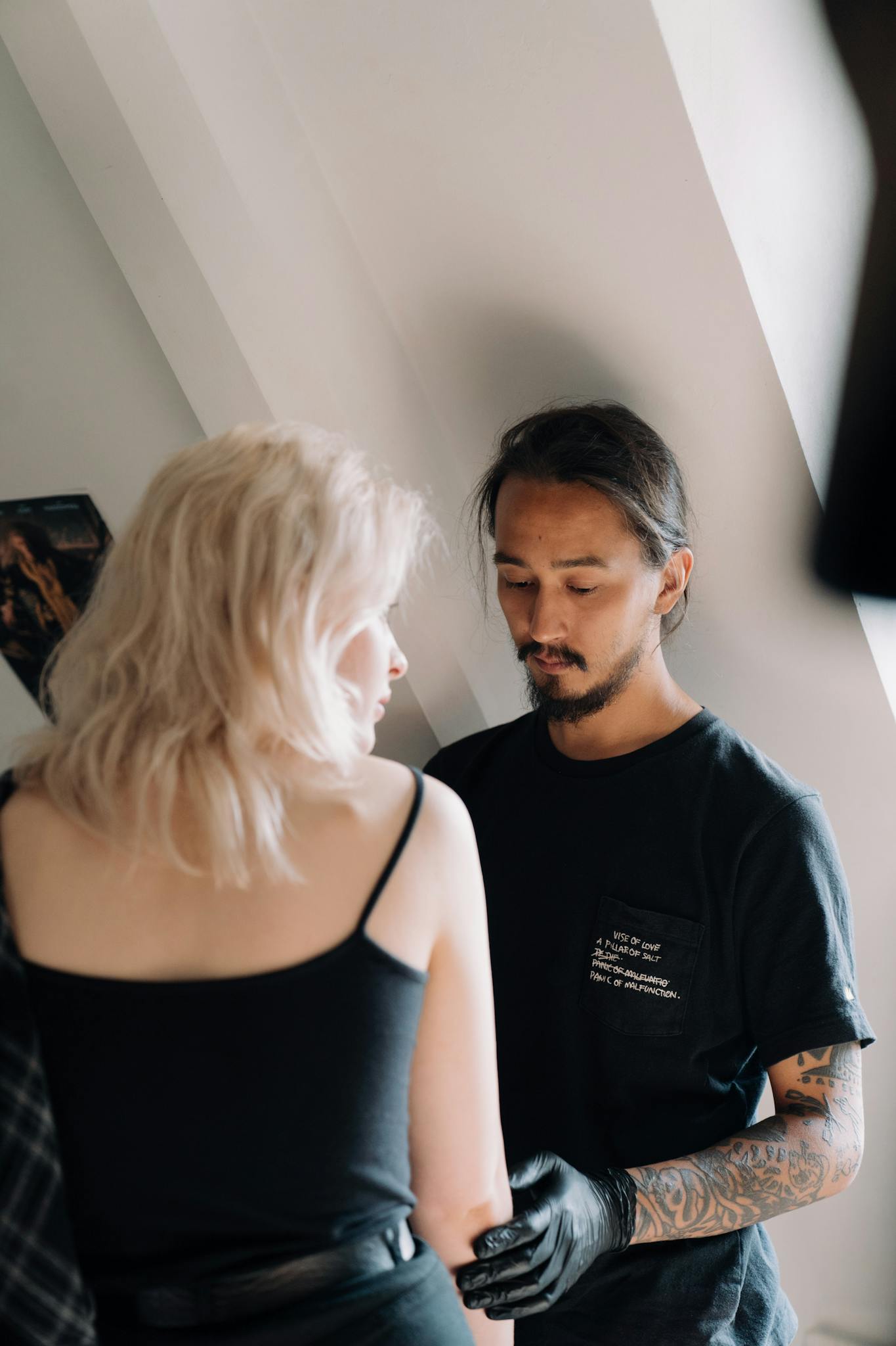 Tattoo artist with gloves tattooing a woman's arm in a modern studio setting.